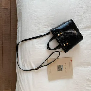 Detail of black glossy patent leather bucket bag with gold rivets and adjustable strap