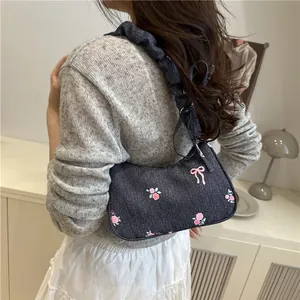 Denim underarm bag with pink rose embroidery and ruffled strap on shoulder