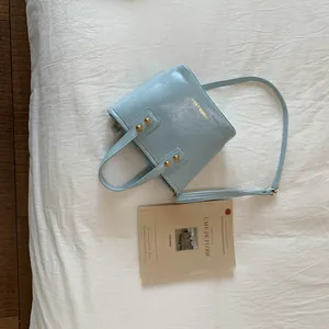 Close-up of light blue leather bucket bag with gold rivets and brand lettering detail
