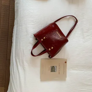 Detail of dark red patent leather bucket bag with gold rivets and brand lettering