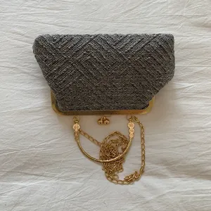 Detailed shot of silver woven clutch bag with gold flower chain and metallic clasp