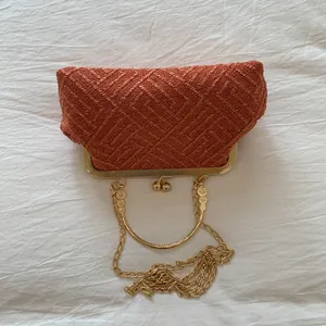 Detail of orange woven evening clutch with gold floral clasp and metal handle