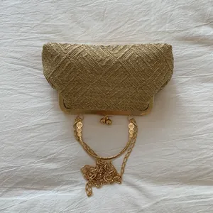 Close-up of golden woven clutch bag featuring floral embossed metal handle and clasp