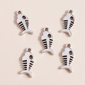 Five vintage silver alloy fish bone charms for DIY jewelry making on beige background