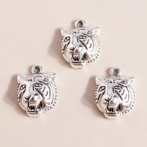 Three antique silver tiger head charms for DIY jewelry making on a beige background
