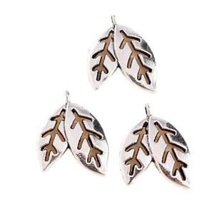 Detailed view of silver hollow leaf charms with intricate patterns and top hanging loops