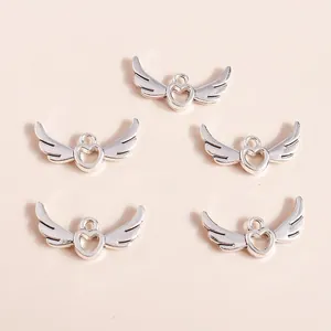 Five silver hollow heart angel wing charms for DIY jewelry making displayed on beige background