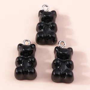 Close-up of three black gummy bear resin pendants with silver jump rings on pink background