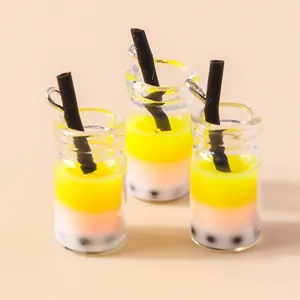 Detail van drie miniatuur bubble tea bedeltjes met gele vloeistof en metalen ringen