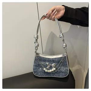 Détail du sac en jean bleu foncé avec nœud argenté et chaîne de perles décorative