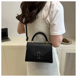 Detail showing elegant trapezoid black shoulder bag with gold hardware on a desk