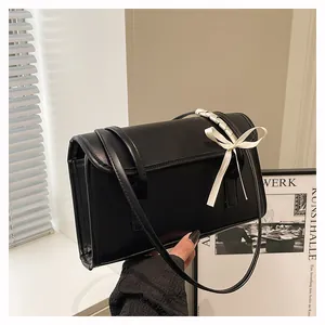 Detail of matte black rectangle shoulder bag featuring a cream ribbon bow on the handle