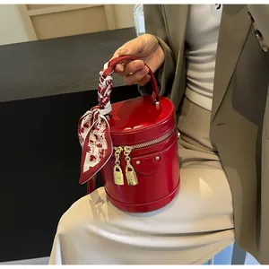 Macro detail of red bucket bag featuring gold hardware and silk scarf wrap on handle