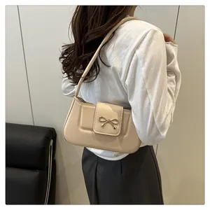 Détail d'un sac baguette beige avec boucle nœud doré porté sur l'épaule d'un mannequin