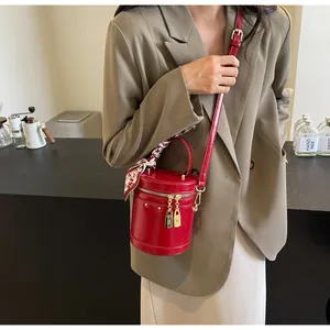 Detail of red cylindrical bucket bag with silk scarf and gold lock charms on model