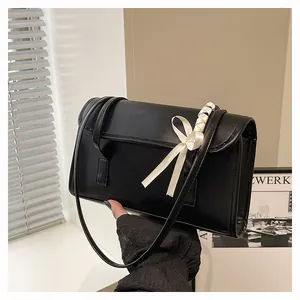 Detail of black faux leather shoulder bag with white satin bow decoration on strap