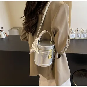 Detail of silver cylindrical bucket bag with metallic finish and decorative silk scarf
