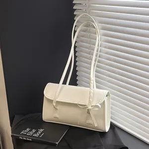 Chic beige faux leather shoulder bag with bow detail and long strap on black desk