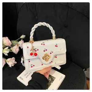 Détail du sac à main cerise avec boucle fleurie et poignée en corde torsadée