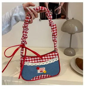 Detalle del asa plisada y el lazo de cuero rojo en el bolso con estampado de cuadros