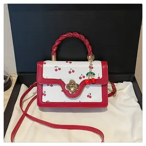 Détail du sac blanc à motif cerise avec poignée tissée et fermoir fleur dorée