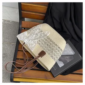 Detailansicht der beigen Strohtasche mit weißer Spitzenschleife und braunem Ledergriff