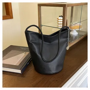 Détail du sac seau en cuir grainé noir avec pendentif chaîne argentée sur table en bois