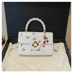 Détail du sac blanc à motifs cerises avec fermoir fleur dorée et charm de cerise