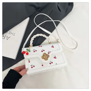 Détail du petit sac bandoulière à motif cerise, poignée tressée et fermoir doré