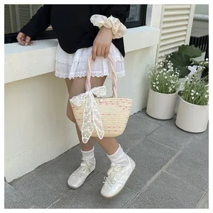 Detalle de bolso tipo cubo de paja beige con puntos de colores y lazo grande de encaje