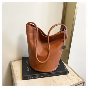 Detail of caramel brown litchi grain leather bucket bag with silver chain pendant accessory