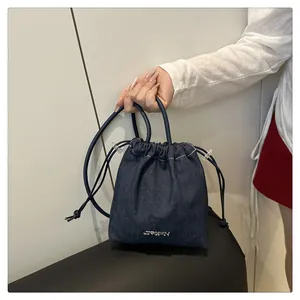 Dettaglio della borsa a secchiello in denim blu con coulisse e logo metallico sul davanti