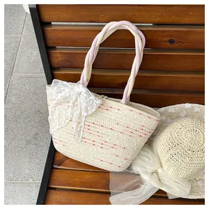 Detalle del bolso de paja tipo cubo con rayas rosas y un gran lazo de encaje blanco