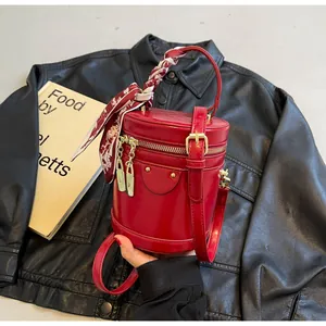 Detail of red bucket bag with gold hardware and decorative silk scarf on handle