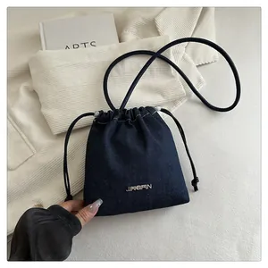 Dettaglio della borsa a secchiello in denim blu scuro con coulisse e logo in metallo