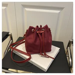 Detail of burgundy faux suede bucket bag with gold ring hardware and drawstring texture