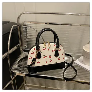 Detailansicht der Muscheltasche mit Kirschmuster, schwarzen Akzenten und Goldreißverschluss