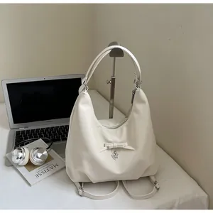 Detail of white multi-functional bag with bow and heart charm on a minimalist desk