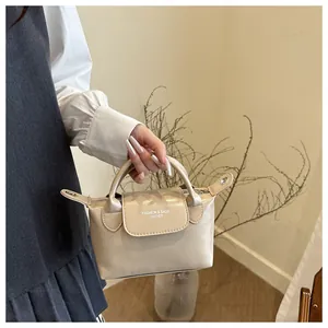 Vue détaillée d'un sac à main beige en cuir avec texte embossé tenu par un mannequin chic