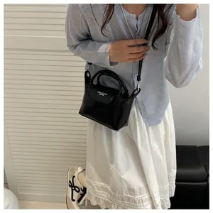 Détail du sac à main noir en cuir verni brillant avec texte blanc et double poignée haute