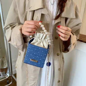 Detail of blue denim bucket bag featuring large pearl handle and drawstring inner liner