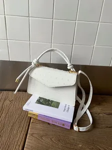 Détail de la texture cuir d'autruche blanc et des ferrures dorées d'un petit sac à main