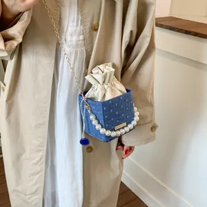 Detail of blue denim bucket bag with pearl handle and golden chain on beige coat
