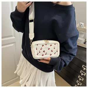 Close-up of white crossbody bag with red cherry prints and adjustable wide shoulder strap