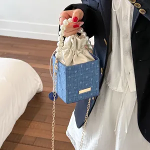 Close-up of blue denim bucket bag with pearl handle, gold chain, and drawstring lining