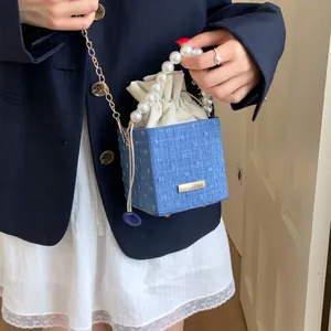 Detail of blue denim bucket bag with pearl handle and metallic chain strap closeup