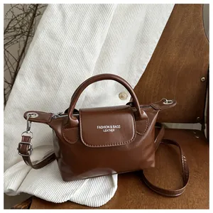 Détail du mini sac à main en cuir marron foncé avec poignée et logo blanc sur chaise en bois