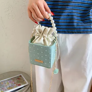 Detail of light green bucket bag with floral texture, pearl handle and gold chain strap