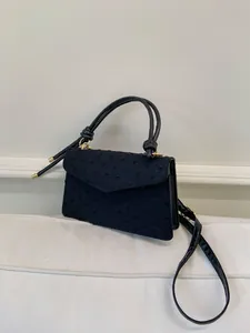 Détail du sac noir en tissu texturé avec fermoir doré et poignée nouée élégante