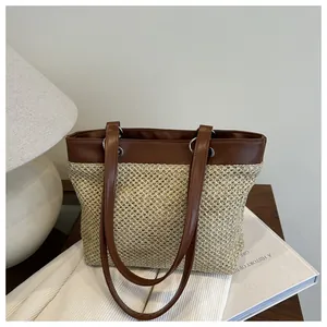 Detail of woven tote bag showing straw texture and brown leather strap on wooden desk